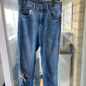 Blå Perfect Jeans från Gina Tricot - Snygga blå jeans från Gina Tricot, modell Perfect Jeans. Klassisk femficksdesign med slitning och hål på ena knät .