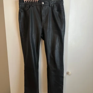 Svarta skinnbyxor från H&M, strl 40 - svarta skinnbyxor från H&M i storlek 40. Byxorna har raka ben och normal passform. De är tillverkade i syntetmaterial med skinnlook och har knapp- och dragkedjestängning framtill.