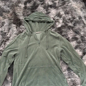 Grön frottéhoodie från Dobber - Mysig grön hoodie från Dobber i frotté med huva, dragsko och halv dragkedja. Tröjan har en stor magficka och långa ärmar, perfekt för chill dagar. Enkel och stilren design som funkar året runt.