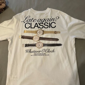 Vit t-shirt med klockmotiv och text - Storlek M men passar mig perfekt och har storlek S!! Nypris köpt för 700kr mitt pris 300 Vit t-shirt med tryck av tre klockor och texten 'Late again? CLASSIC' på ryggen samt 'Late again, my friend' på bröstet. Skön passform och rund halsringning. Perfekt för dig som gillar coola statement-plagg och humoristiska detaljer.