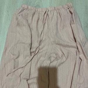 Ljusrosa vida linnebyxor med snörning - Säljer ett par ljusrosa linnebyxor med avslappnad passform och breda ben. Byxorna har resår i midjan och snörning för extra komfort. Materialet är luftigt och har en lätt struktur, perfekt för varmare dagar.