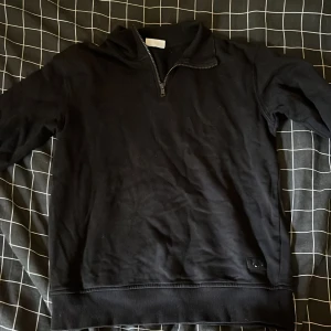 Svart half zip tröja från Kappahl - Svart långärmad tröja från Kappahl med half zip-dragkedja vid halsen. Tröjan har en enkel och stilren design med ribbade muddar vid ärmslut och nederkant. Perfekt för lager-på-lager och chill dagar.