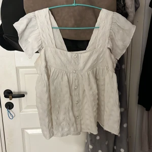 Vit blus med volangärm - Supersöt vit blus från ASOS DESIGN med breda axelband och volangärmar. Blusen har knappar framtill och är gjord i ett krinklat bomullstyg som ger en chill och luftig känsla. Perfekt för dig som gillar romantiska och trendiga vibes 🤍