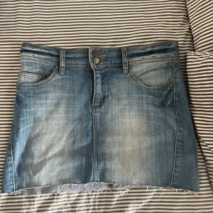 Blå jeanskjol från KappAhl, stl 36 - Säljer en snygg blå jeanskjol från KappAhl i storlek 36. Kjolen har rå kant nertill, klassiska fem fickor och coola detaljer på bakfickorna. Perfekt för dig som gillar trendig stil.