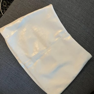 Vit kortkjol i skinnimitation från H&M - Säljer en vit kortkjol från H&M Divided i skinnimitation med croco-mönstrad yta. Kjolen har en tight passform och dragkedja i sidan för enkel påtagning. Perfekt för dig som vill sticka ut med en cool och trendig look.