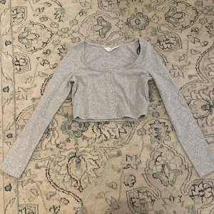 Grå croppad kofta med knappar H&M - Säljer en ljusgrå croppad kofta från HM i storlek 146/152. Koftan har en urringad neckline och passar perfekt med ett fint linne under❣️