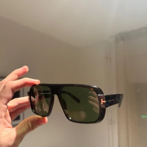Tom Ford Turner solglasögon brun - Säljer ett par Tom Ford Turner TF1101 solglasögon med rektangulär form och gröna linser. Bågarna är brunmelerade med klassisk T-detalj i silver på sidorna. Kommer med originalfodral och box. Perfekt för dig som gillar exklusiv design. Kvitto medföljer ej men äktahetsbevis finns!!! 