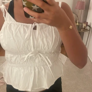 Vit volangig linnetopp med knyt -  Alldrig andvänt den tidigare. Jätte fin sommar topp till sommaren. Parfekt topp till stranden. Supersöt vit linnetopp med smala axelband, volangkant nertill och två knytband framtill. Toppen har rynkade detaljer och en luftig, flowy passform som känns perfekt för varma dagar. Materialet är tunt och mjukt, vilket gör den extra bekväm och fräsch. 