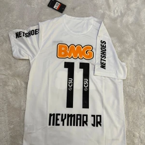 Santos Neymar JR fotbollströja Nike - Snygg vit Santos fotbollströja från Nike med Neymar JR och nummer 11 på ryggen. Tröjan har korta ärmar, tryckta sponsorer som BMG och Netshoes, samt Santos klubbmärke på bröstet. Tillverkad i lätt Dri-Fit material som andas, perfekt för match eller träning.