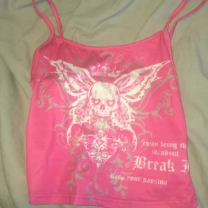 Rosa linne med dödskalletryck från SHEIN - Säljer ett rosa linne från SHEIN i storlek XS med smala axelband och ett stort tryck framtill med dödskalle, vingar och text. Toppen har en edgy vibe och är gjord i stretchig polyesterblandning. Perfekt för dig som gillar statement-plagg och coola detaljer./ ai skrev ❤️🙏
