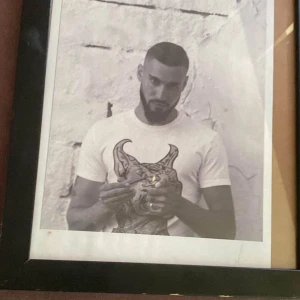 Haval tavla  - Det här är en inramad svartvit fotografi av en person med en t-shirt med ett konstnärligt tryck. Perfekt för dig som gillar unik väggkonst och vill ha något coolt och personligt i ditt rum. Bilden har en modern känsla och passar bra i ungdomliga miljöer.