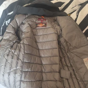 Svart dunjacka från Parajumpers - Säljer en svart dunjacka från Parajumpers, modell Last Minute. Jackan är quiltad med horisontella sömmar, har huva och dragkedja framtill. Klassisk PJS-patch på ärmen. Perfekt för kalla dagar och riktigt snygg streetstil.