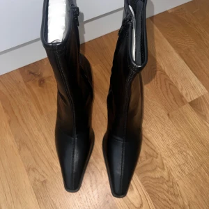 Svarta stövletter med spetsig tå från NA-KD - Snygga svarta stövletter från NA-KD med spetsig tå och smal klack. Skorna har dragkedja på sidan och är tillverkade i syntetmaterial med en slät finish. Perfekt för dig som gillar en edgy och stilren look. Klackhöjden ger en elegant siluett.