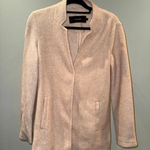 Ljusrosa kappa från Vero Moda - Stilren ljusrosa kappa från Vero Moda med rak passform och diskret krage. Jackan har dolda knappar framtill och två fickor på sidorna. Tillverkad i mjukt och skönt material som ger en clean och klassisk look. Väldigt fint skick!