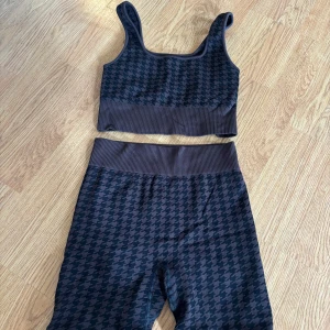 Brunt träningset från NA-KD - Säljer ett snyggt träningset från NA-KD i brunt med mönster. Toppen har breda axelband och ribbad kant nedtill, och tränings shortsen har hög midja med samma ribbade detalj. Materialet är mjukt och stretchigt för en bekväm passform.