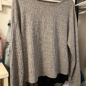 Grå ribbad långärmad tröja - En enkel och stilren grå långärmad tröja med ribbad struktur. Tröjan har en rak passform och är tillverkad i ett mjukt material som känns skönt mot huden. Perfekt att slänga på sig när du vill ha en chill och clean look.