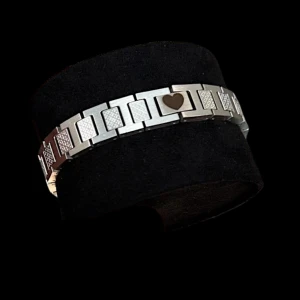 Silverfärgat armband med hjärtdetalj - Snyggt armband i silverfärgad metall med rektangulära länkar och en unik hjärtdetalj i mitten. Vissa länkar har ett diskret mönster som ger extra stilpoäng. Perfekt för dig som gillar stilrena accessoarer med en twist.