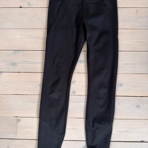 Svarta leggings från Stronger XS - Svarta leggings från Stronger i storlek XS. Tillverkade av 77% återvunnen polyester och 23% elastan för en stretchig och bekväm passform. Hög midja och diskret logga fram.