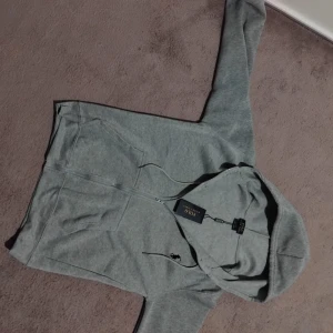 Grå hoodie från Polo Ralph Lauren - Snygg grå hoodie från Polo Ralph Lauren med klassisk svart logga på bröstet. Tröjan har huva med snörning, dragkedja framtill och två fickor. Mjuk bomullskvalitet och ribbade muddar vid ärmslut och nederkant. Perfekt för chill dagar.Storlek S och M