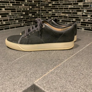 Lanvin uk 9 - Snygga svarta sneakers från lanvin  ovandel i mocka och tåparti i blankt material. Skorna har svarta snören, vit sula och klassisk rund tå. Perfekta för dig som gillar stilrena och minimalistiska skor med en twist.