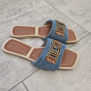 Blå denim sandaler med guldkedja - Snygga sandaler i blå denim och brunt konstläder med fyrkantig tå och platt sula. aldrig använt jag säljer den eftersom jag fick fel storlek. Jag har en till i guldig färg och den finns i min profil 