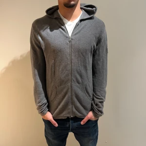 Grå cardigan/hoodie från Ljung Marcus Larsson - Säljer en stilren grå hoodie från Ljung Marcus Larsson i storlek M. Tröjan har dragkedja framtill, huva och två fickor. Materialet är mjukt och stickat, perfekt för chill dagar. Passformen är normal och ärmarna är långa. NYPRIS:1699Kr Mitt pris:499Kr
