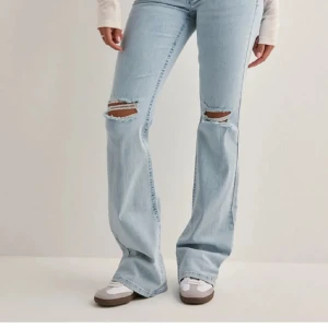 Bootcut ljusblå jeans med slitningar - Snygga ljusblå bootcut jeans med slitna hål på knäna och broderade detaljer på bakfickorna. Jeansen har hög midja och är tillverkade i klassiskt denimtyg. Perfekta för dig som gillar en avslappnad och trendig look.