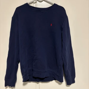 Mörkblå sweatshirt från Polo Ralph Lauren - Snygg mörkblå sweatshirt från Polo Ralph Lauren med klassisk röd logobroderi på bröstet. Tröjan har rund hals, långa ärmar och är tillverkad i mjuk bomull. Perfekt för dig som gillar stilrena och tidlösa plagg.(använt några få gånger) köptes för 2100, drf är de lägsta 500kr.