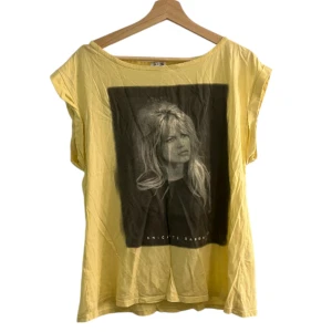 Gul t-shirt med Brigitte Bardot-tryck - Gul t-shirt med avslappnad passform och stort svartvitt tryck av Brigitte Bardot på framsidan. T-shirten har korta ärmar och bred halsringning.