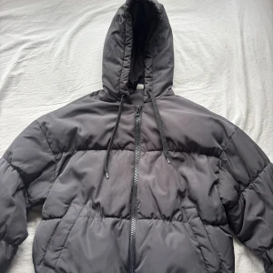 Svart pufferjacka från H&M Divided XS - Säljer en svart pufferjacka från H&M Divided i storlek XS. Jackan har huva med snörning, dragkedja framtill och ribbade muddar vid ärmsluten. Perfekt för kalla dagar och har en oversized vibe.