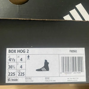 Adidas Box Hog 2 boxningsskor svart/vit - Adidas Box Hog 2 boxningsskor i svart med klassiska vita ränder på sidorna. Skorna har hög modell med snörning hela vägen upp, platt sula i vitt och meshmaterial för bra ventilation. Perfekt för dig som vill ha lätt och smidig sko i ringen. Använda en gång av dottern. 