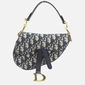 Dior Saddle Bag i blått monogram - Ikonisk Dior Saddle Bag med blått och beige monogrammönster, guldfärgade metalldetaljer och justerbar axelrem i skinn. Väskan har den klassiska sadelformen och ett stort D-hänge framtill. Perfekt statement piece för dig som vill sticka ut.