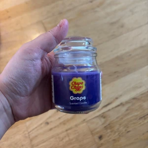 Chupa Chups Grape Scented Candle - Chupa Chups Grape Scented Candle i glasburk. Lila färg, doft av druva. Burken och veken ser ut att vara i nyskick utan synligt slitage eller defekter. Perfekt för att skapa en härlig atmosfär hemma.