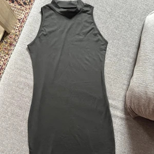 Svart ärmlös kortklänning - Snygg svart ärmlös klänning med hög krage och figurnära passform. Klänningen är kort och har en stilren, minimalistisk look som passar perfekt för dig som gillar enkel men trendig stil.