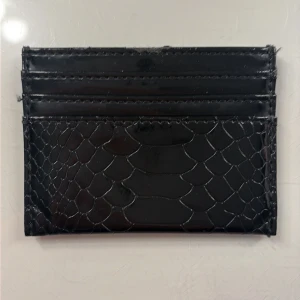 Svart plånbok i croco-mönstrat skinn - Slimmad svart plånbok med croco-mönstrad yta i glansigt skinn. Perfekt för kort och sedlar, stilren och enkel att ha i fickan. Ger en lyxig känsla med sitt reptil-inspirerade mönster och passar dig som gillar minimalistisk design.