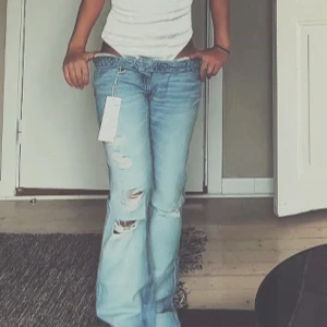 Ljusa bootcut jeans från Gina Tricot - Säljer ett par ljusblå jeans från Gina Tricot i bootcut-modell med slitna detaljer och hål. Perfekt för dig som gillar en avslappnad och trendig stil.