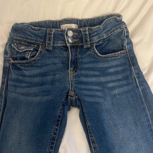 Blå jeans från Gina Tricot - Snygga blå jeans från Gina Tricot i storlek 152. Bruna sömmar med dubbla knappar i midjan och raka ben. Bra i skick och sitter väldigt skönt❣️