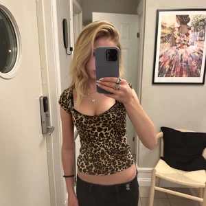 Leopardmönstrad tight topp - Säljer en snygg leopardmönstrad topp med korta ärmar och djup urringning. Modellen är tight och figurnära, perfekt för dig som gillar att sticka ut. Materialet känns mjukt och stretchigt, vilket gör den bekväm att bära. Passar dig som vill ha en cool och trendig look.