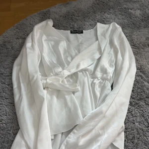 Vit omlottblus från Missay - Säljer en vit omlottblus från Missay med långa ärmar och knytband i midjan. Blusen har en v-ringad omlottfront och är gjord i ett glansigt, mjukt material som ger en lyxig känsla. Perfekt att styla med jeans eller kjol för en fräsch look.