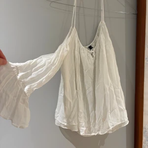 Vit blus med snörning och volangärm - Säljer en vit blus med tunna axelband, snörning framtill och volangärmar. Blusen har en luftig och flowy passform med lätt transparent material som ger en bohemisk vibe. Perfekt för dig som gillar romantiska detaljer och en avslappnad stil.