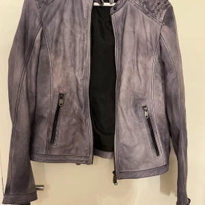 Grå skinnjacka från Frontrow - Snygg grå skinnjacka från frontrow med flätade detaljer på axlarna och dragkedjor vid fickor och ärmslut. Jackan har fläckar (se bild) som jag inte vet om dom går bort eller inte för har inte provat, men kan försöka om du är intresserad. Står ingen storlek men skulle gissa att den är xs/s.