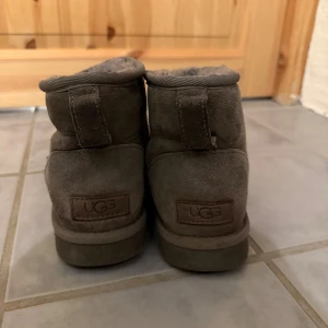 Gråa UGG  - Mysiga gråa UGGs  med låg skaft och rund tå. Utsidan är i mjuk mocka och insidan är fodrad med fluffigt material som håller fötterna varma. Perfekt för kalla dagar och har en platt sula för skön komfort. Storlek 38!