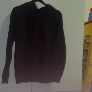 Svart hoodie med huva - En klassisk svart hoodie med huva och långa ärmar. Perfekt för dig som gillar en enkel och stilren look. Tröjan har en normal passform och är tillverkad i ett mjukt material som känns skönt mot huden.