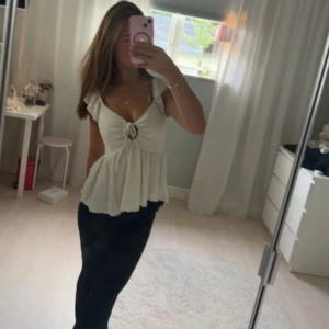 Vit blus med volang - Supersöt vit blus med knyt framtill. Toppen har volangdetaljer vid axlarna och är ärmlös med lätt rynkad, flowy nederdel. Perfekt för sommarens alla tillfällen och har en feminin v-ringad design. Materialet känns mjukt och luftigt.