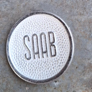 SAAB 96 emblem 1960 tal till sidoventilation - Klassisk SAAB-emblem i metall Passar till äldre SAAB-bilars sidoventilationsplåt, perfekt för samlare eller renovering. Viss patina och mindre repor syns, men överlag i gott skick. Ger din bil en autentisk vintage-look. Sällsynt idag