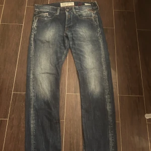 Blå Replay jeans straight fit - Säljer ett par klassiska blå Replay jeans med snyggt slitna detaljer och raka ben. Jeansen har fem fickor, Replay-logga på bakfickan och läderpatch i midjan. Perfekt passform och cool tvätt som ger en avslappnad vibe. W32 L32.