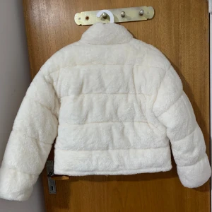 Vit teddyjacka med dragkedja - Supermjuk och fluffig vit teddyjacka med quiltad look och hög krage. Jackan har en rak, lite boxig passform och stängs med dragkedja framtill. Perfekt för att hålla värmen och se stylish ut under kyliga dagar.