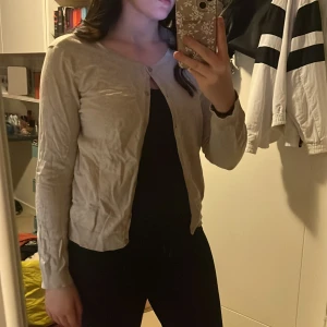 Beige kofta med knappar - Snygg beige kofta med rund hals och knäppning framtill. Långärmad och i ett mjukt, tunt material. 