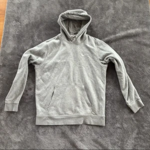 Grå Nike hoodie med huva, storlek L - Säljer en klassisk grå hoodie från Nike i storlek L. Tröjan har huva med snörning, magficka och diskret Nike-logga på bröstet. Tillverkad i mjuk bomullsblandning med 80% bomull och 20% polyester för extra komfort. Perfekt för chill dagar eller när du vill ha en enkel streetstyle.