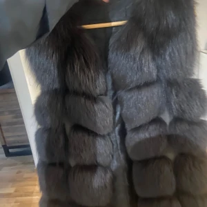 Svart fluffig pälsväst - Säljer en riktigt maffig och lång pälsväst i svart nyans. Västen har breda, fluffiga paneler som ger en lyxig och trendig look. Perfekt för dig som vill sticka ut och hålla värmen med stil. För snabb affär kan gå ner i pris